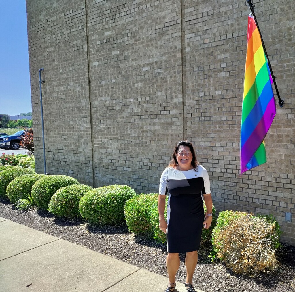 Becky standing near the Pride Flag at AP Membrane Solutions factory in St. Louis, MO, in June 2022.