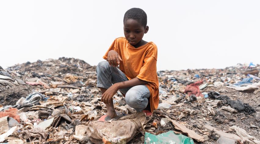 Photo: Child sitting on an African garbage dump, looking at the plastic waste.